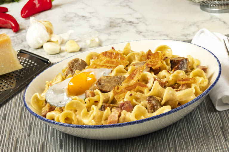 Brio's Campanelle Carbonara in a bowl with fresh ingredients in the background